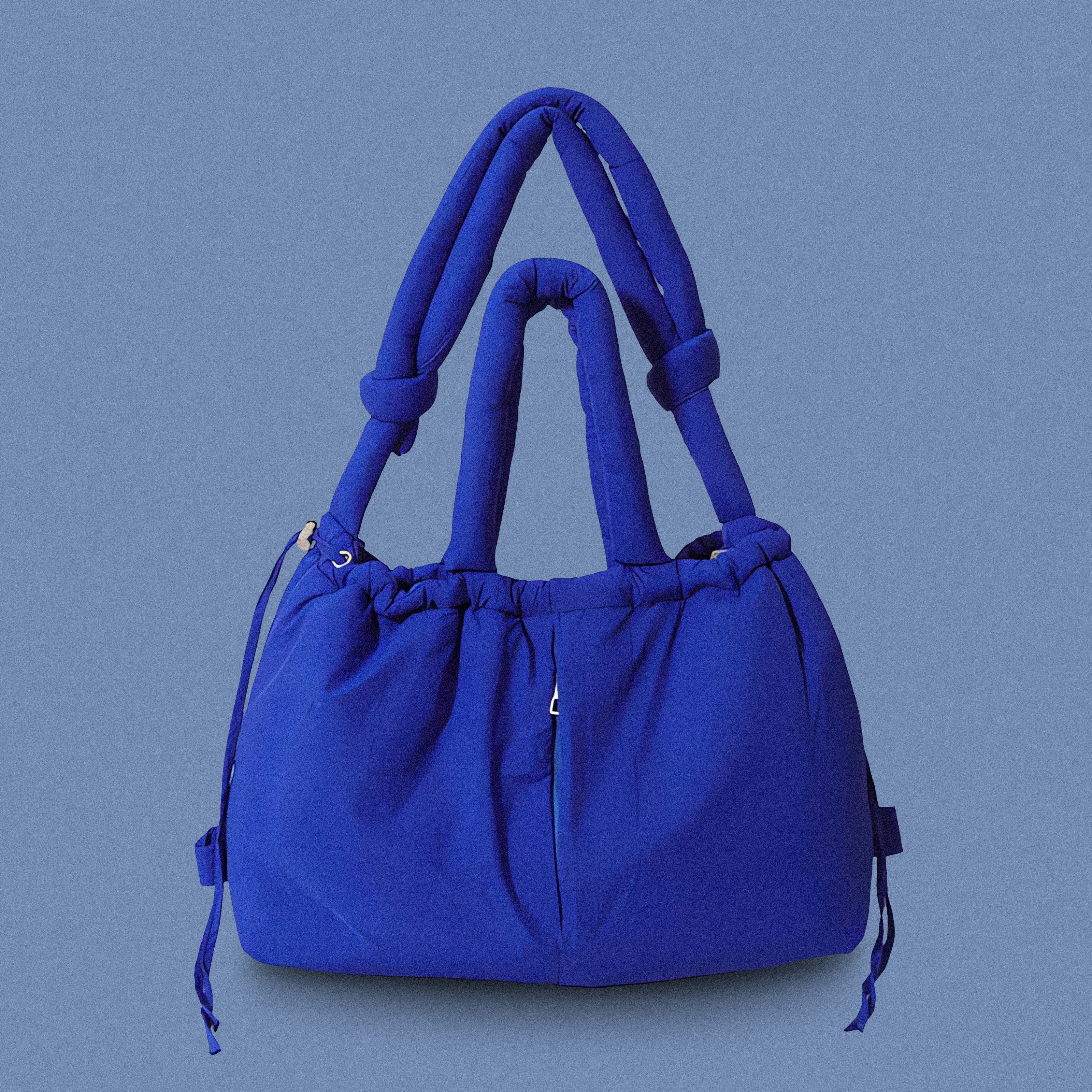 PLSH blue women’s designer puffer handbag on a blue background