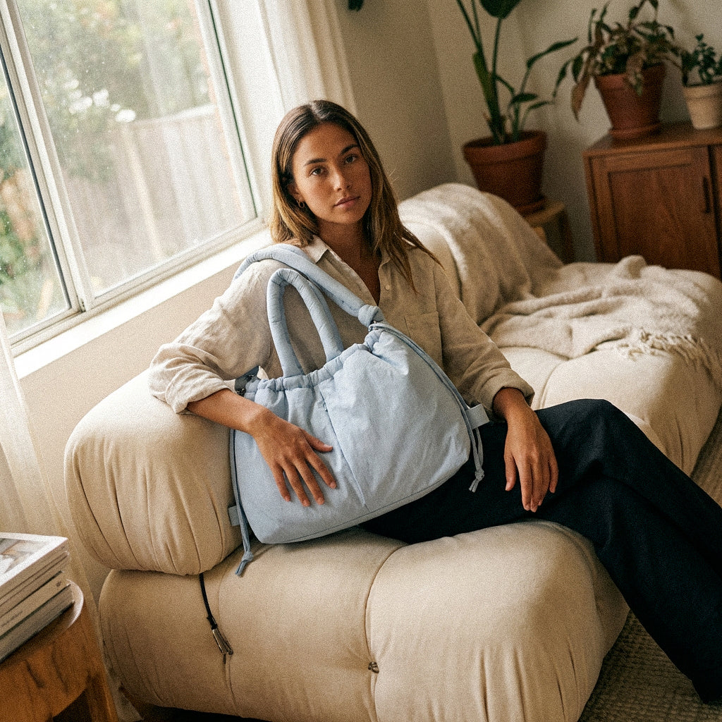 Woman holding a PLSH blue women's designer handbag in a cozy living room