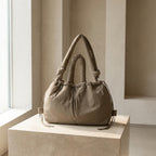 PLSH beige women's designer handbag on a light-colored pedestal against a neutral background