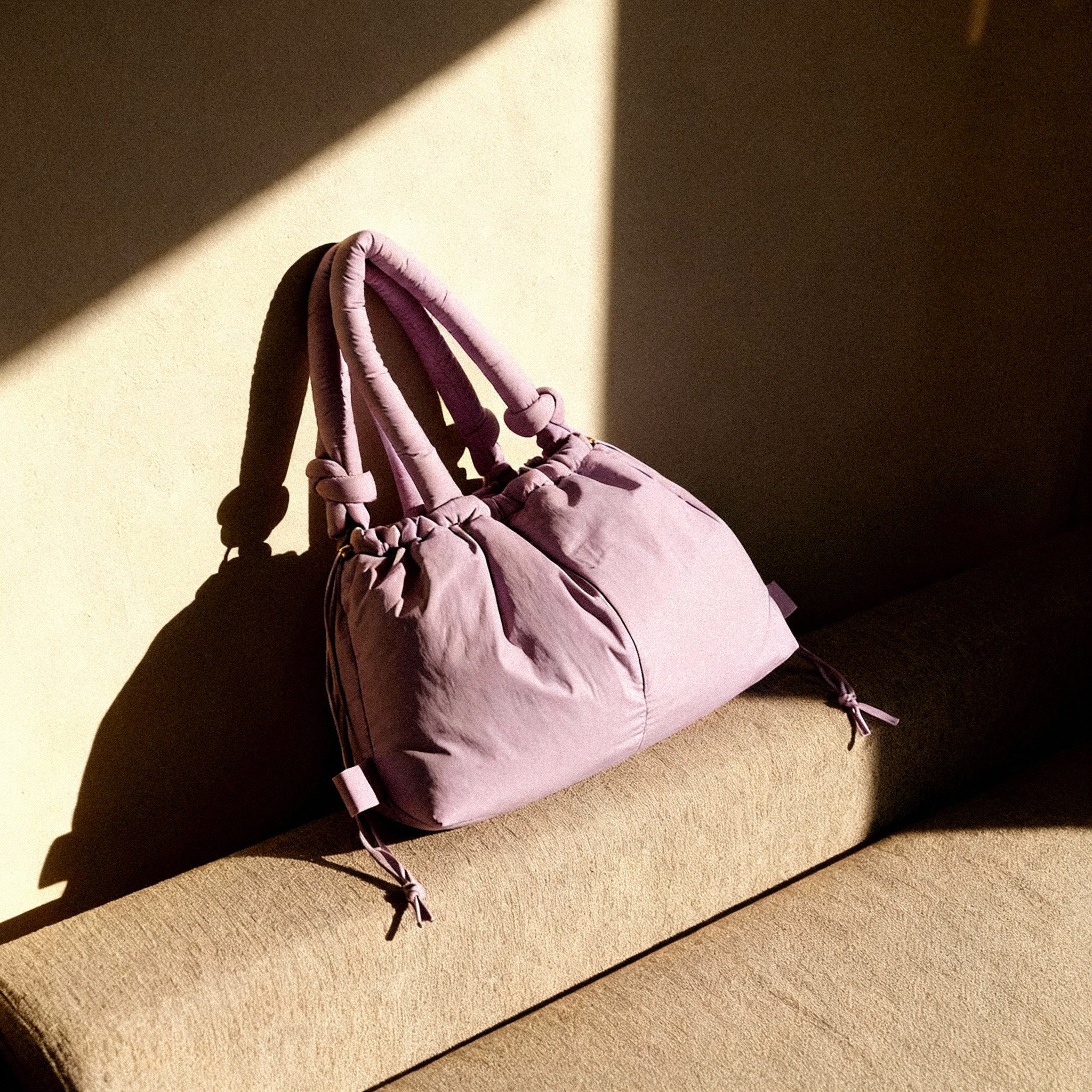 PLSH pink women's designer handbag on a beige surface with a soft shadow