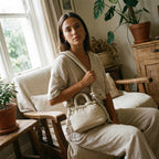 Woman sitting in a cozy room wearing a PLSH designer handbag with plants and wooden furniture