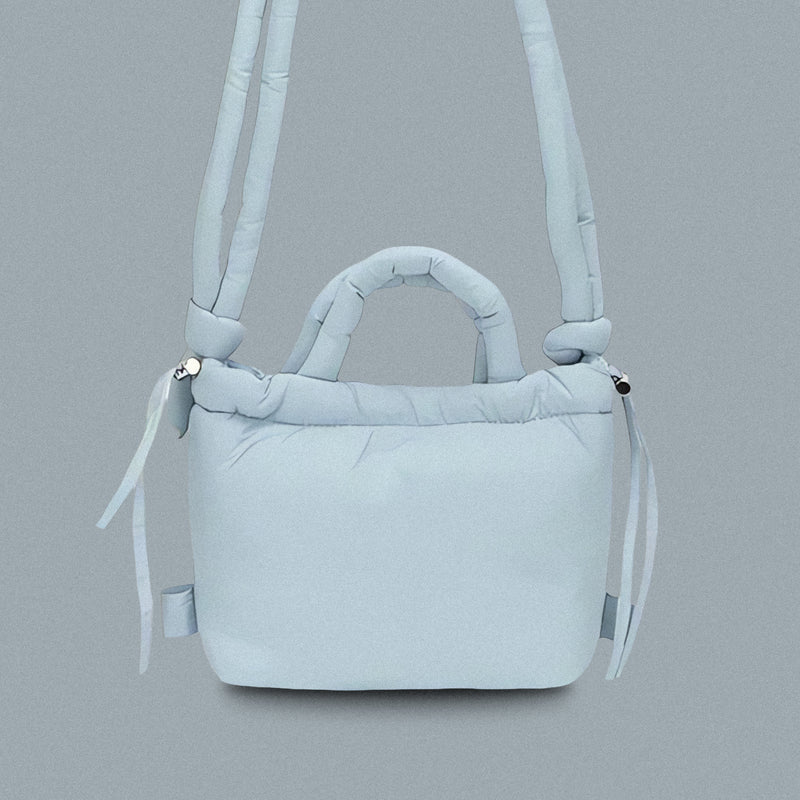 PLSH baby blue women’s designer puffer handbag on a blue background