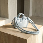 PLSH light blue women's designer handbag with a long strap on a stone surface