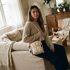 Woman sitting on a couch holding a PLSH beige designer handbag in a cozy living room