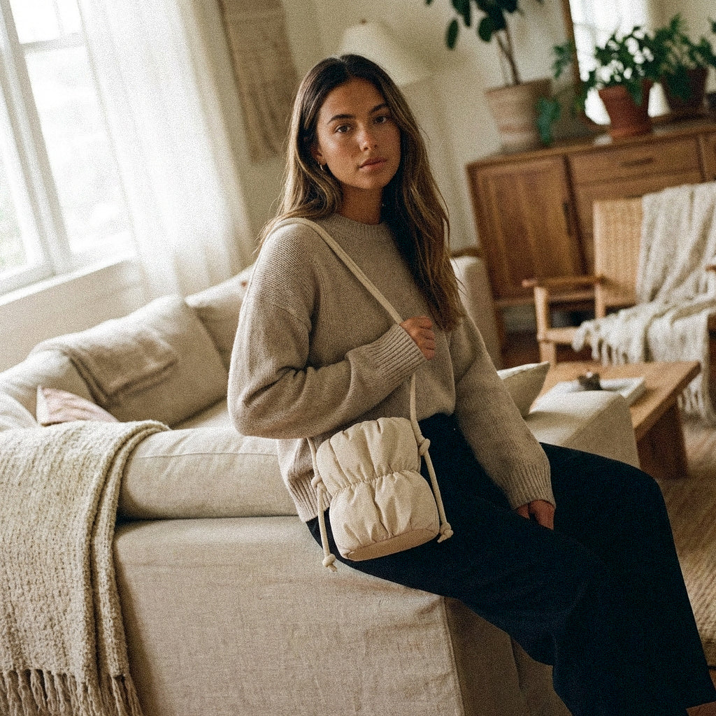 Woman sitting on a couch holding a PLSH beige designer handbag in a cozy living room