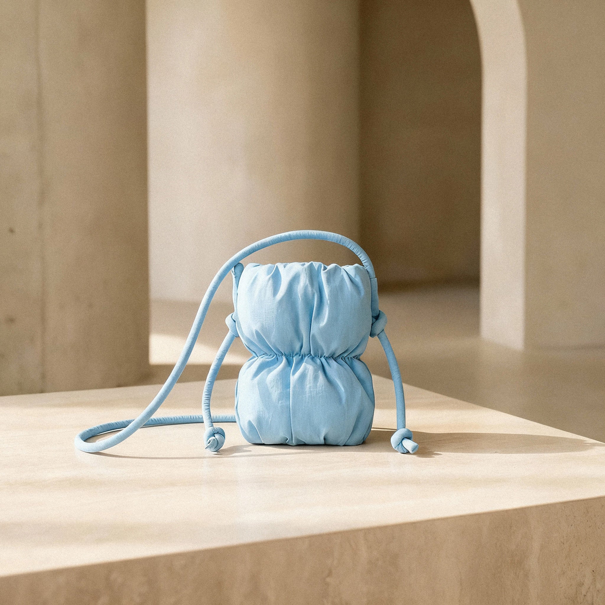 PLSH blue women's designer handbag on a beige surface with a neutral background