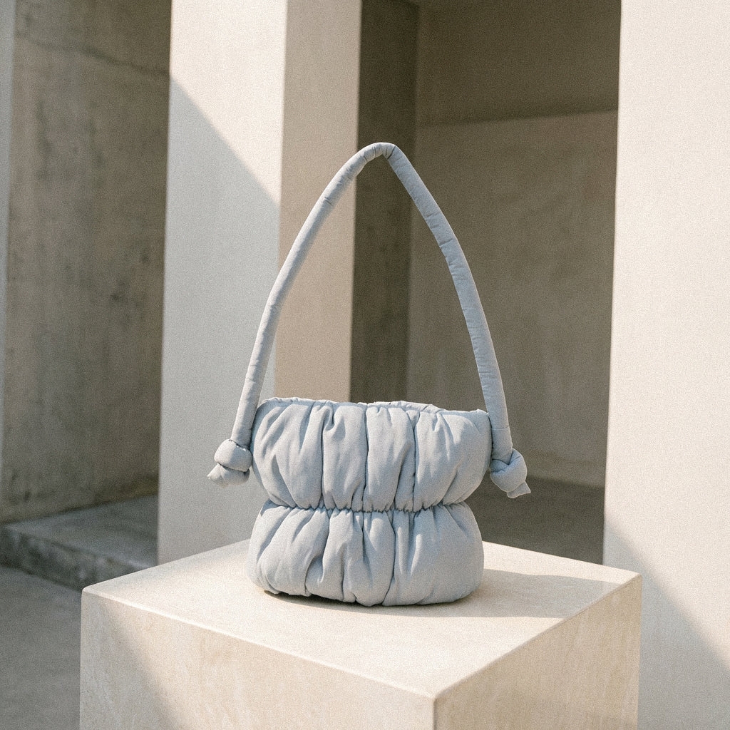 PLSH baby blue women's designer handbag on a stone pedestal with a neutral background