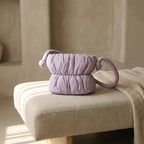 PLSH lilac women's designer handbag on a beige upholstered bench