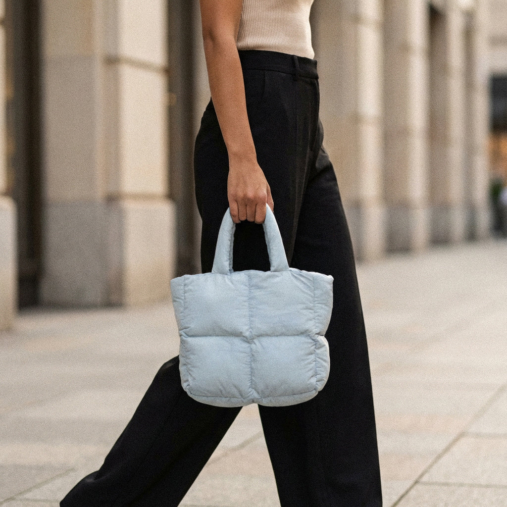Woman holding a PLSH light blue designer quilted handbag on a city street