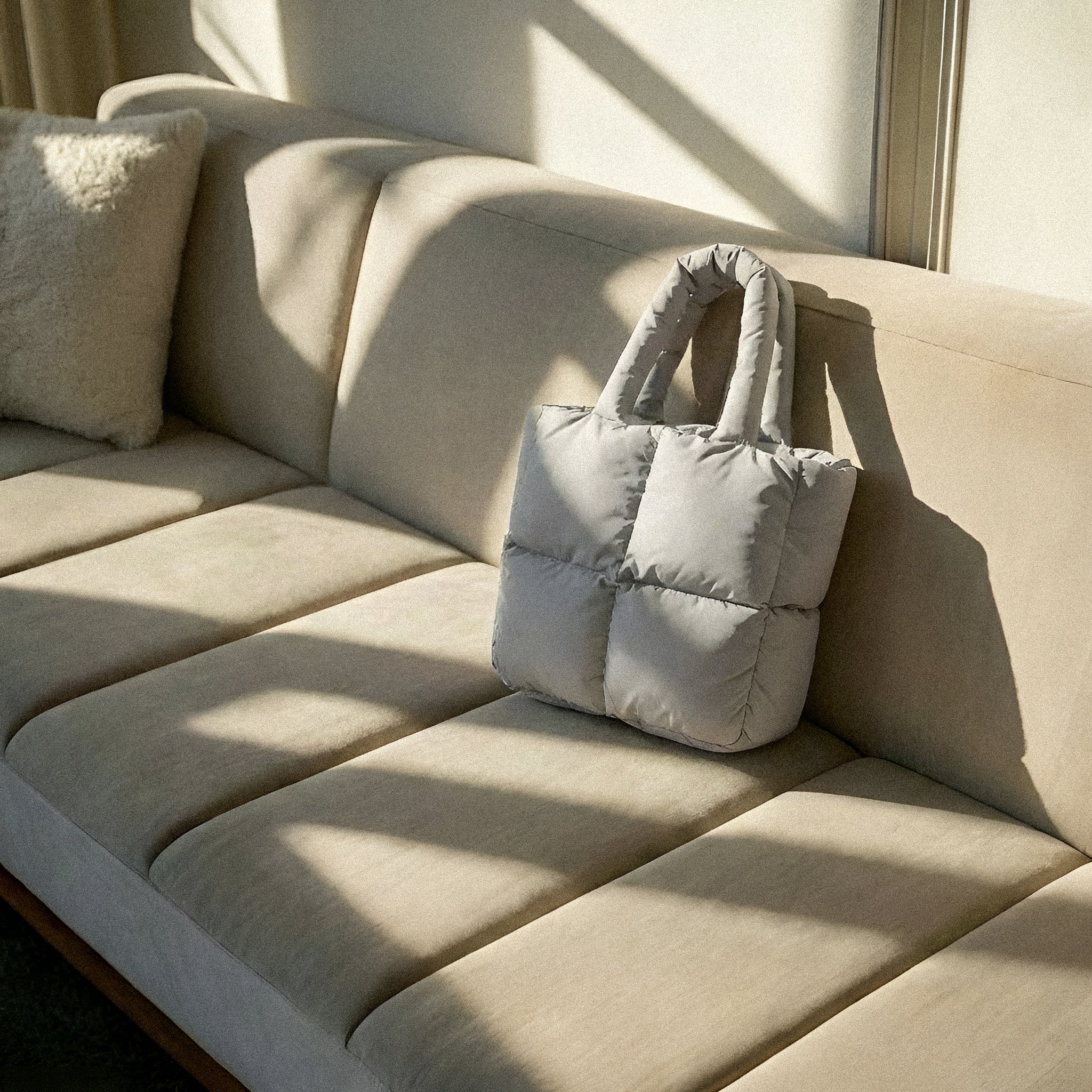 PLSH beige women's designer puffer handbag on a beige sofa with sunlight casting shadows