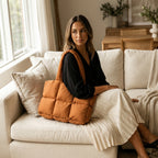 Woman sitting on a couch holding a PLSH designer orange puffer handbag in a cozy living room
