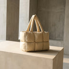 PLSH beige women's designer quilted handbag on a concrete surface with a neutral background