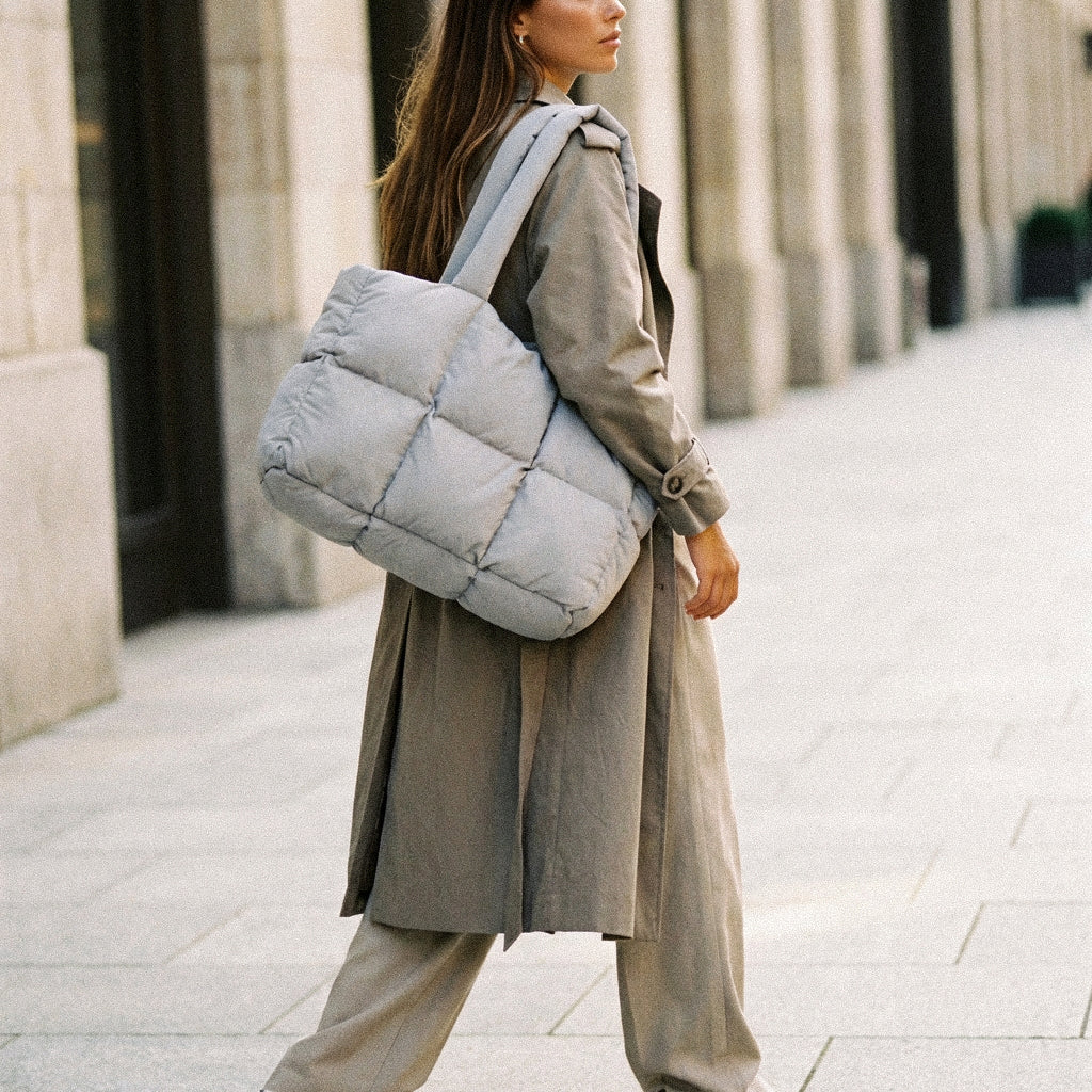 Woman holding a PLSH designer light blue puffer handbag on a city street
