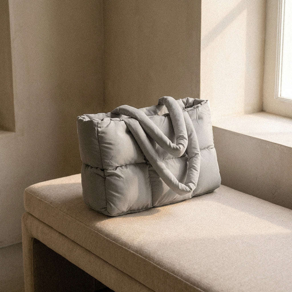 PLSH gray women's designer quilted handbag on a beige cushion in a softly lit room