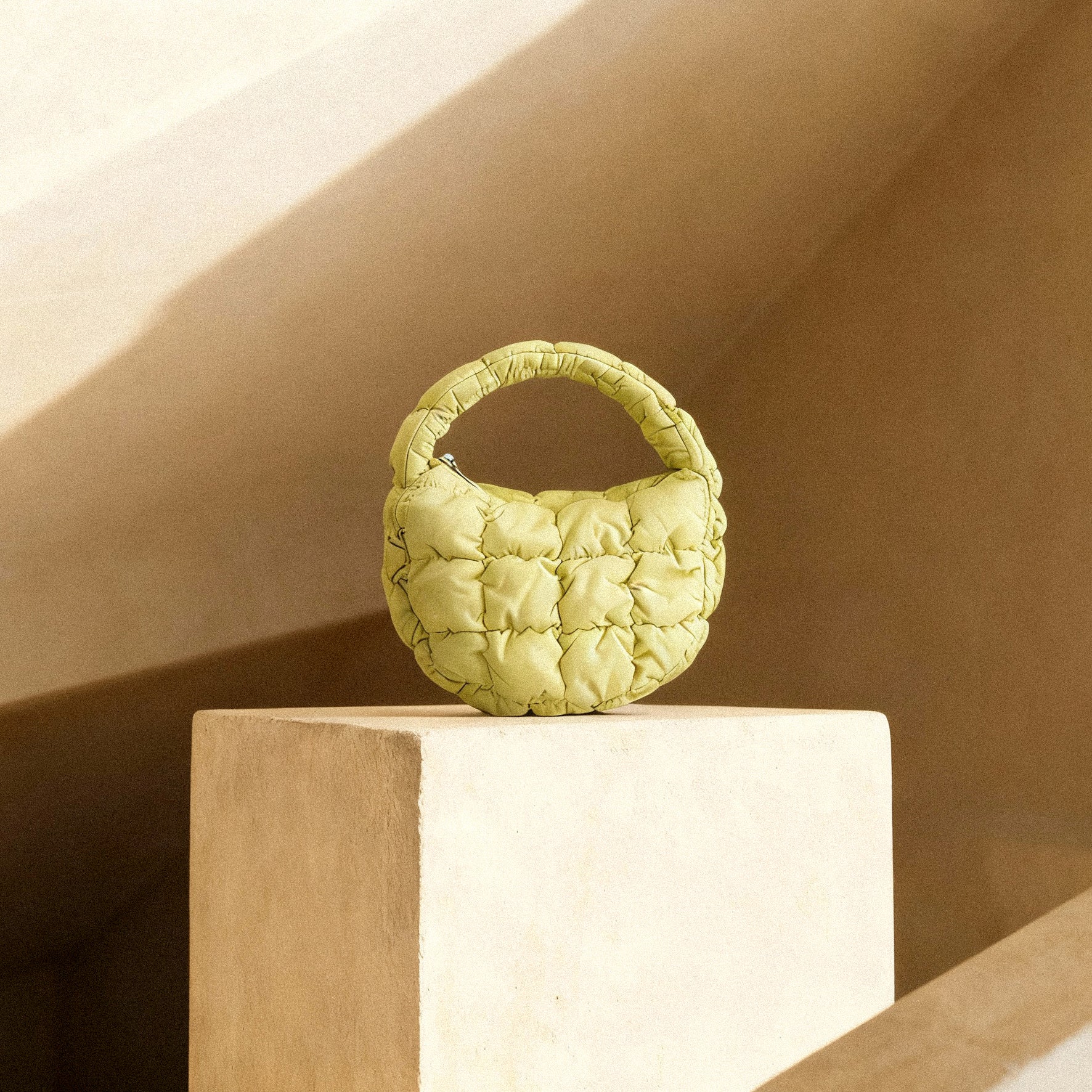 PLSH lime green women's designer quilted handbag on a white pedestal against a beige background