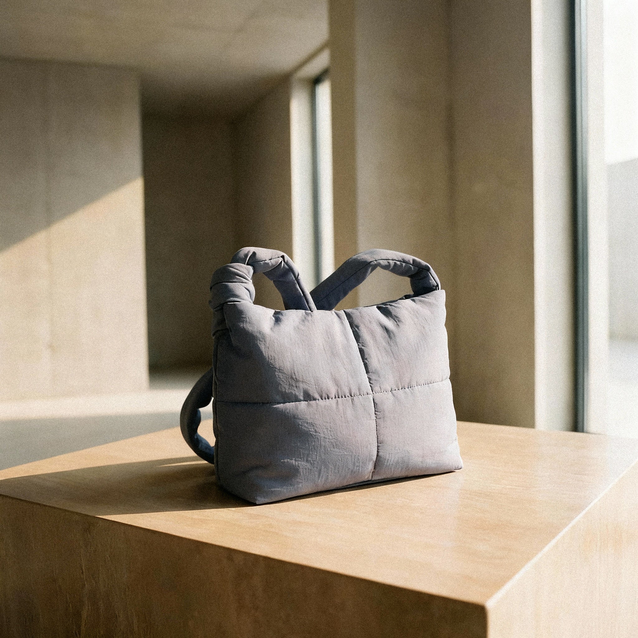 PLSH gray women's designer handbag on a wooden surface with a minimalistic background