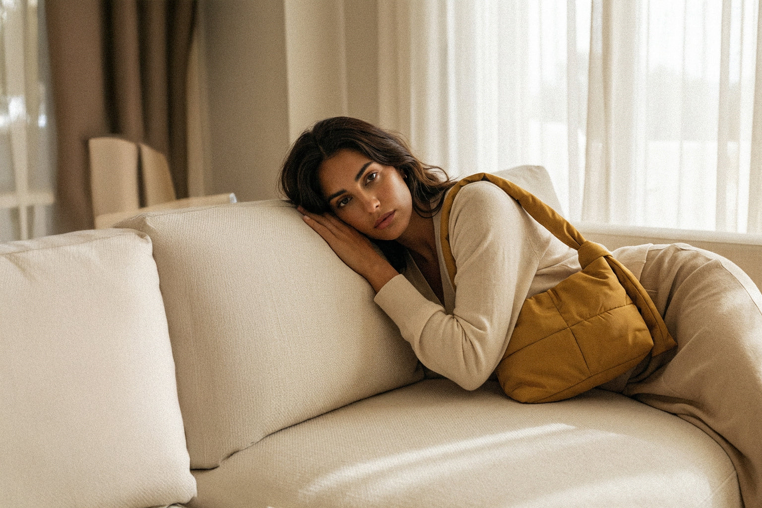 Woman sitting on a beige couch in a softly lit room with a PLSH yellow designer handbag