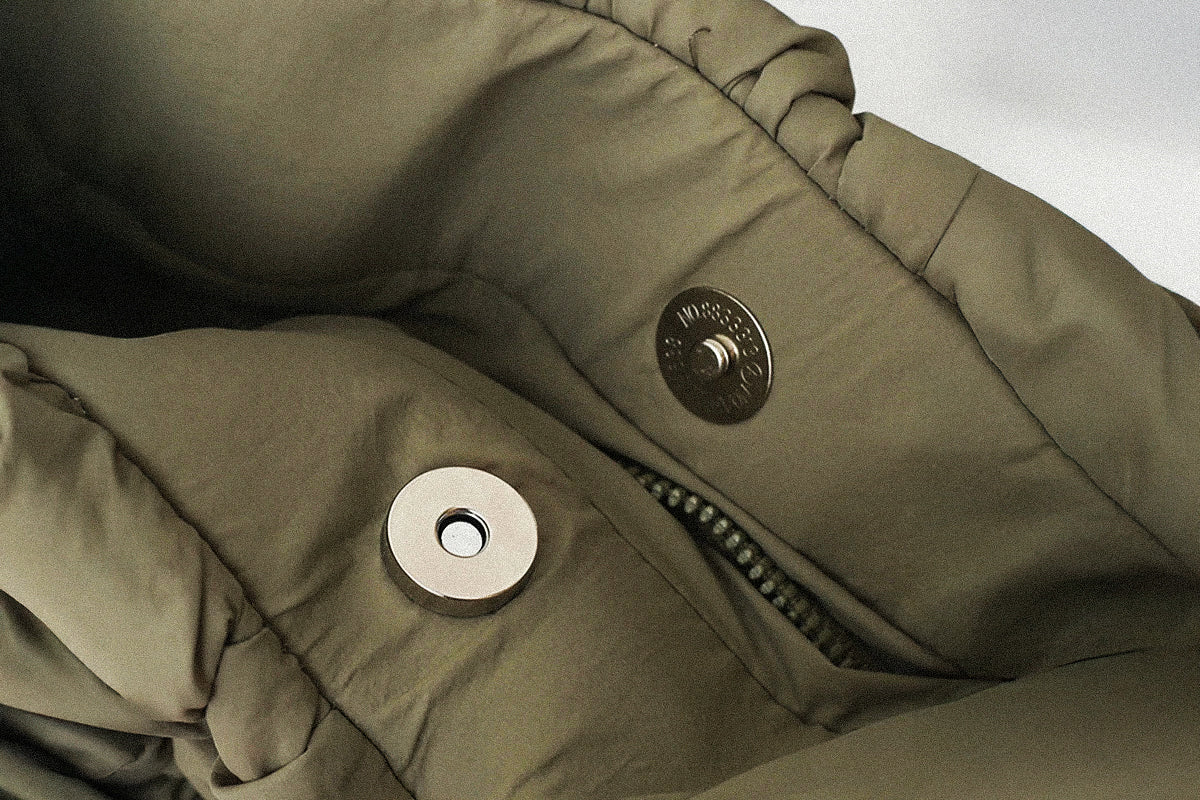 Close-up of a green PLSH women's designer handbag with buttons and a zipper on a light gray background