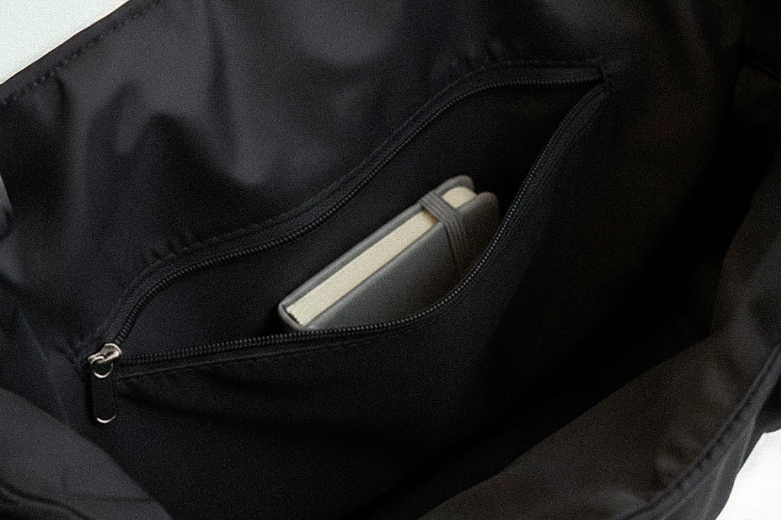 Black PLSH women's designer handbag with a pocket containing a notepad on a light gray background