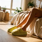 Woman wearing PLSH women's premium lime green slippers in a cozy bedroom with sunlight streaming in