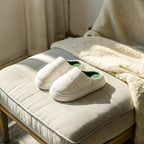 Pair of PLSH white women's premium slippers with green interior on a cushioned bench